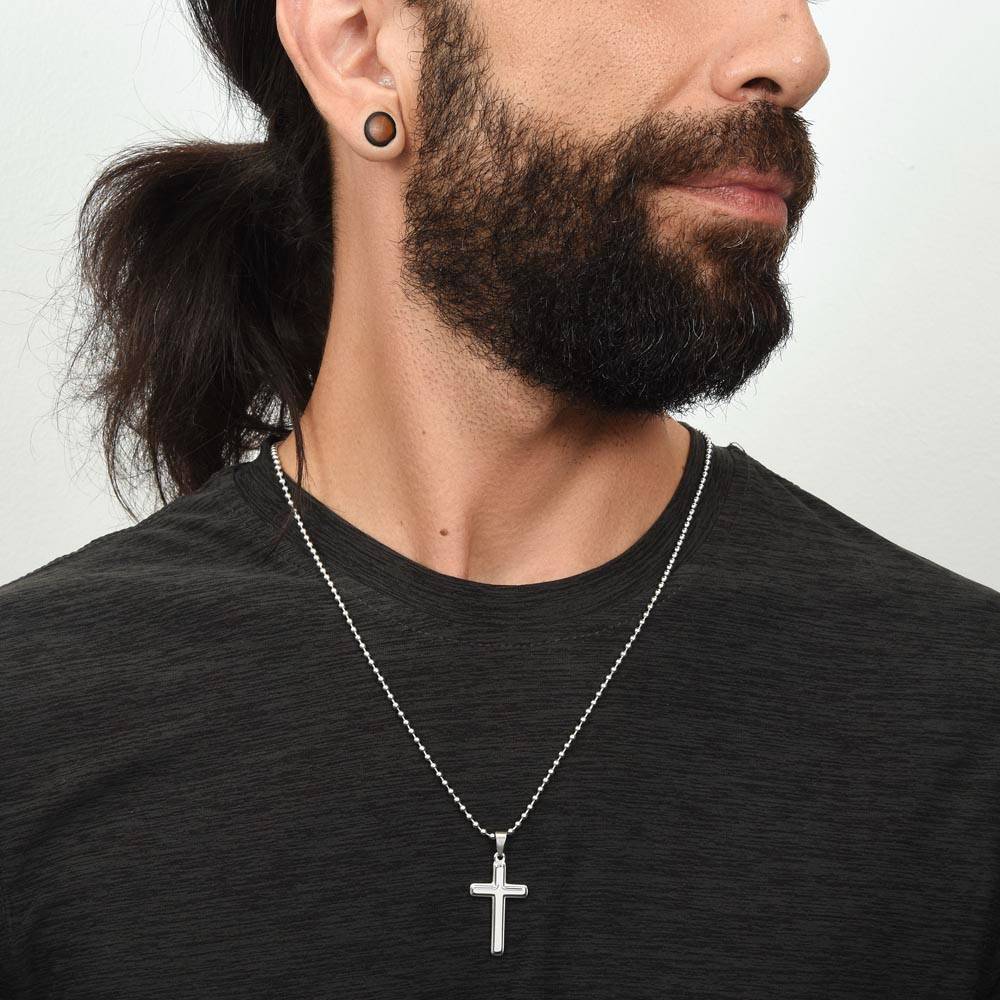 Man wearing a black shirt with a silver cross necklace against a plain background